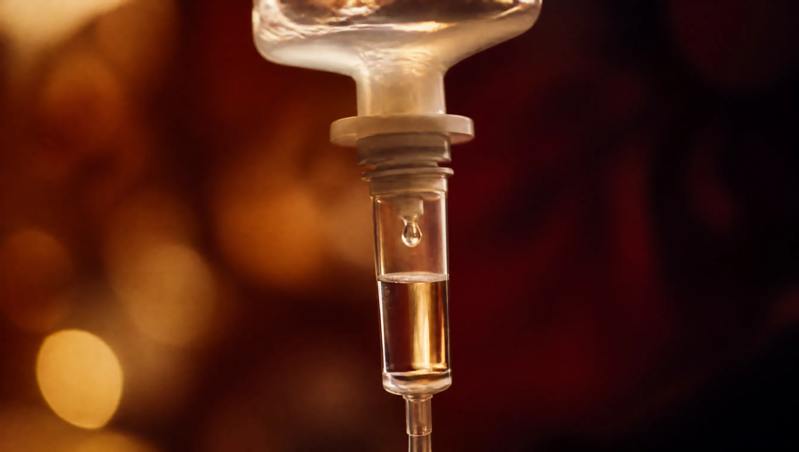 A close-up of an IV drip chamber with a single drop forming.